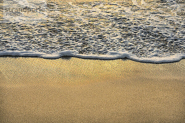 Nahaufnahme einer Meereswelle auf Sand bei Sonnenuntergang