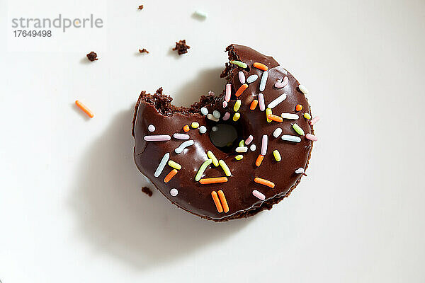 Draufsicht auf einen teilweise aufgegessenen Donut mit Schokoladenglasur und Streuseln