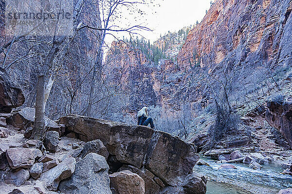 Vereinigte Staaten  Utah  Zion-Nationalpark  ältere Wanderin ruht sich im Winter auf einem Felsen über dem Virgin River im Zion-Nationalpark aus