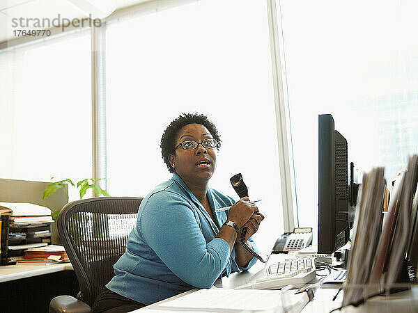 Geschäftsfrau sitzt am Schreibtisch mit Telefon