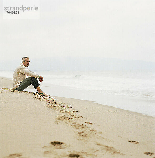 Mann sitzt am Strand und blickt auf das Meer