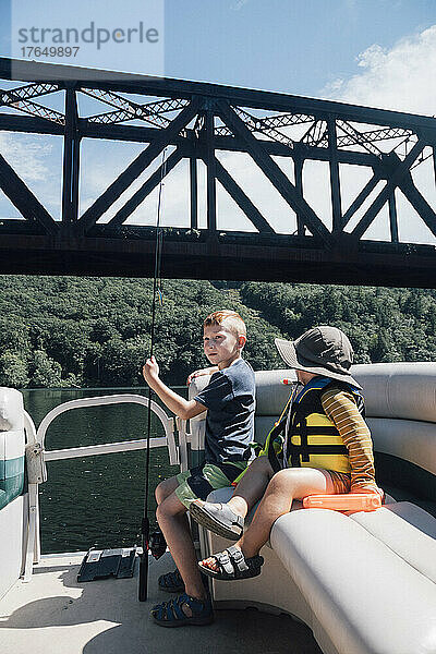Jungen sitzen an einem sonnigen Tag im Boot mit Angelrute