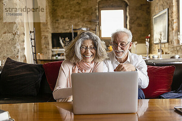 Glückliche Frau mit Laptop sitzt mit Mann auf Sofa im Boutique-Hotel