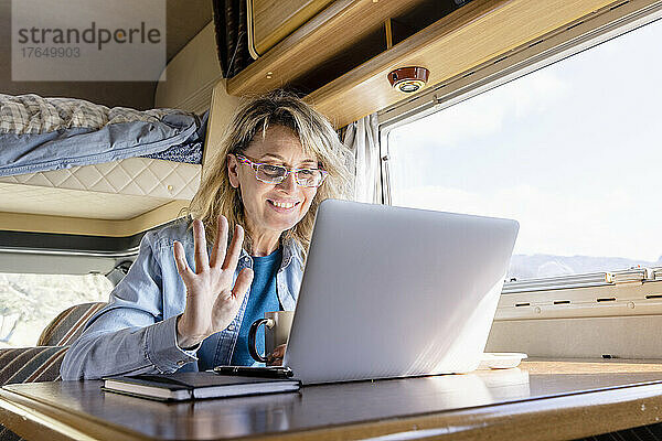 Lächelnde Frau winkt bei Videoanruf über Laptop im Wohnmobil
