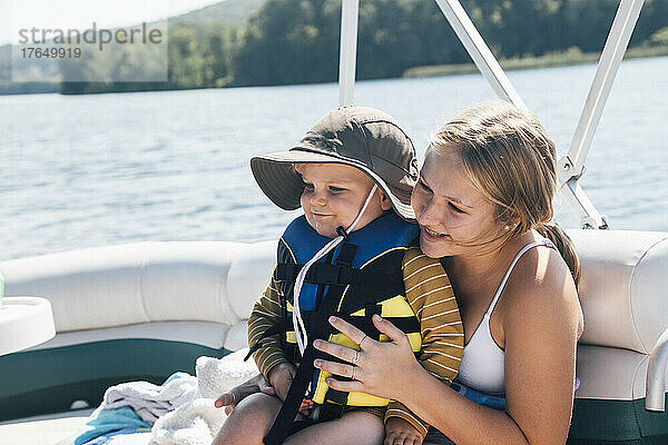 Niedlicher kleiner Junge sitzt auf dem Schoß einer Frau auf einem Flussboot