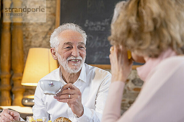 Smiling man holding coffee cup looking at woman sitting in boutique hotel