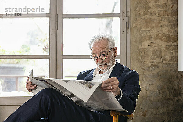 Älterer Mann liest Zeitung und sitzt zu Hause vor dem Fenster