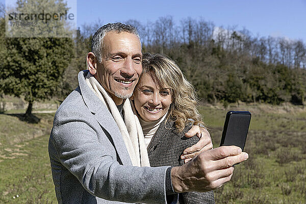 Smiling mature couple with arm around taking selfie on smart phone