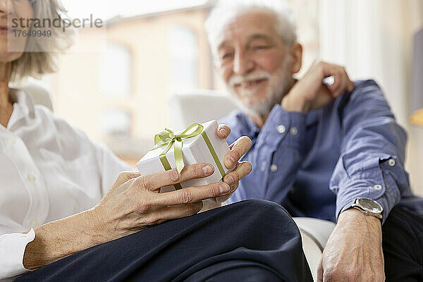 Glückliche ältere Frau mit Geschenkbox sitzt neben Mann in Hotelwohnung