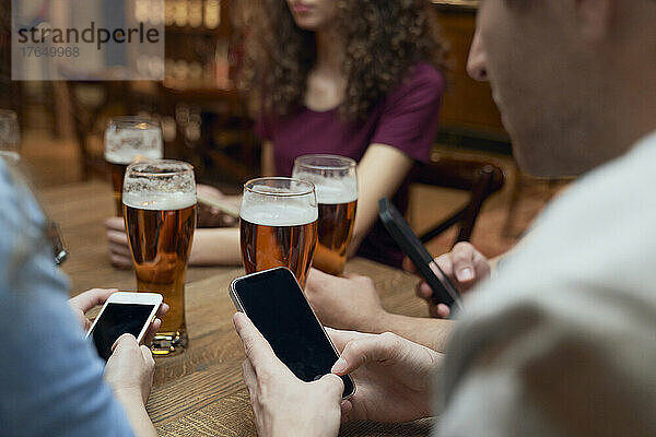 Freunde trinken Bier und nutzen Smartphones in einer Kneipe