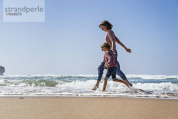 Glückliche Mutter und Tochter laufen an einem sonnigen Tag am Strand im Wasser
