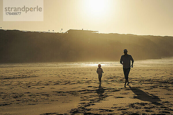 Vater und Tochter laufen bei Sonnenuntergang am Strand