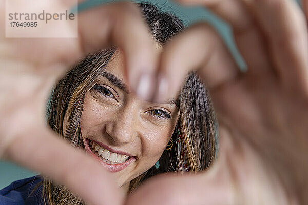 Cheerful young woman making heart shape in front of face