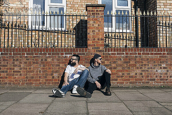 Zwei Männer sitzen auf dem Bürgersteig vor einer Mauer
