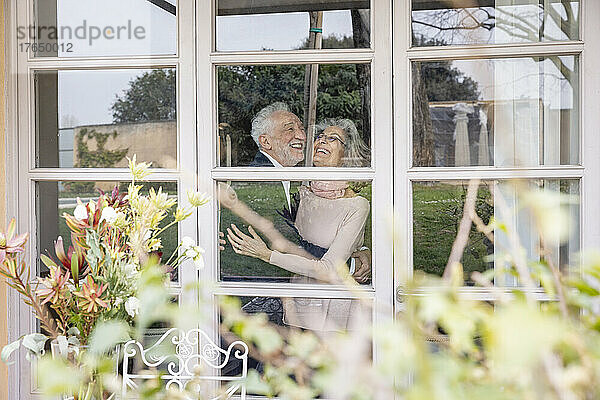 Glückliches älteres Paar  das sich durch das Fenster umarmt