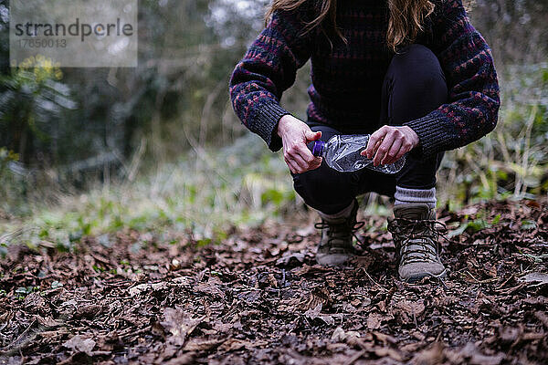 Junge Frau hebt Plastikflasche im Wald auf