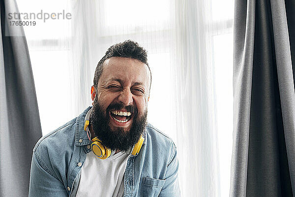 Hipster-Mann mit Kopfhörern lacht zu Hause