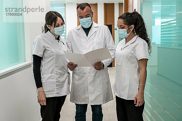 Arzt und Krankenschwestern tragen Schutzmasken und analysieren den medizinischen Bericht im Flur des Krankenhauses