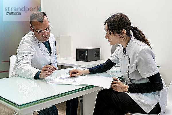 Arzt und Krankenschwester diskutieren am Schreibtisch in der Klinik über den medizinischen Bericht