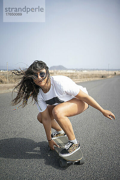 Frau mit zerzausten Haaren fährt an einem sonnigen Tag Skateboard