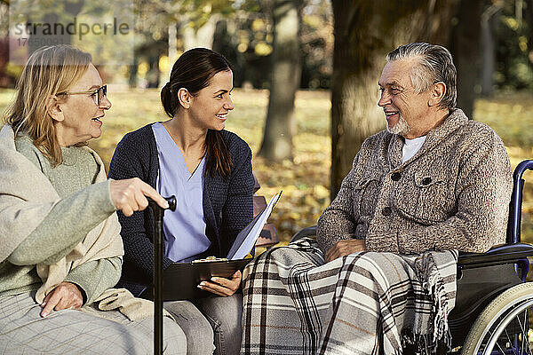 Lächelnde Krankenschwester bespricht Dokumente mit älterem Paar im Park