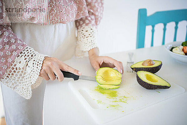 Junge Frau hackt Avocado und steht am Tisch