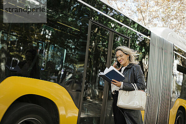 Lächelnde Frau  die mit dem Smartphone telefoniert und im Bus Tagebuch liest