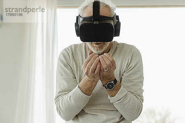 Älterer Mann mit Virtual-Reality-Simulator steht mit gefalteten Händen im Boutique-Hotel