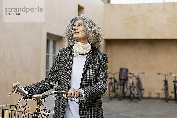 Ältere Frau steht mit Fahrrad vor Gebäude