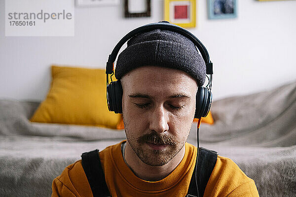 Mann mit geschlossenen Augen hört zu Hause Musik über Kopfhörer