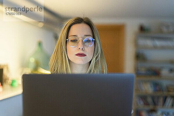 Junge Frau mit Brille arbeitet am Laptop am Tisch