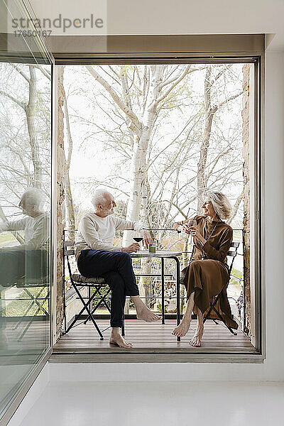 Älteres Paar mit Weingläsern sitzt auf dem Balkon einer Hotelwohnung