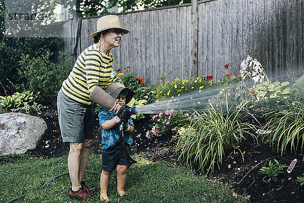 Glückliche Großmutter und Enkel  die gemeinsam Pflanzen im Garten gießen