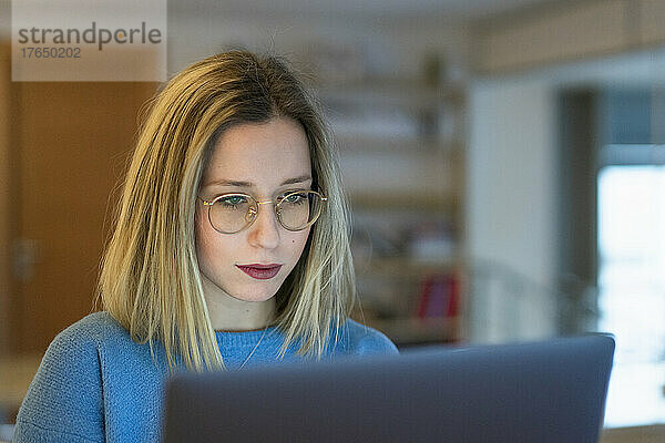 Junge blonde Frau sitzt am Tisch und benutzt Laptop