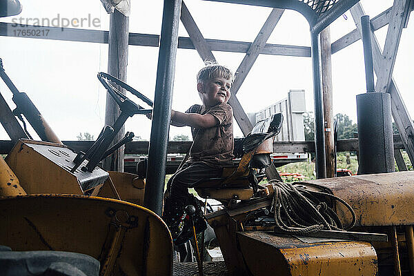 Vorschuljunge sitzt auf Traktor im Bauernhof