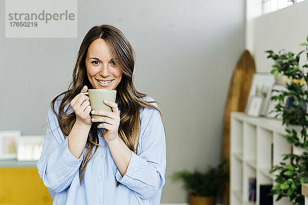 Lächelnde schöne Frau mit Kaffeetasse zu Hause