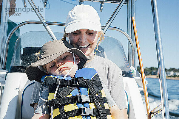 Lächelnde Mutter mit Sohn in Schwimmweste im Schnellboot an sonnigem Tag
