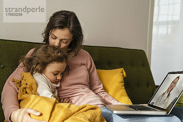 Mutter umarmt kranke Tochter und konsultiert zu Hause online über den Laptop einen Arzt