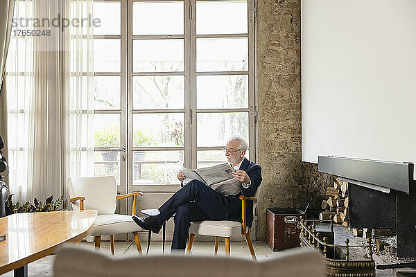 Älterer Mann liest Zeitung und sitzt am Fenster im Wohnzimmer