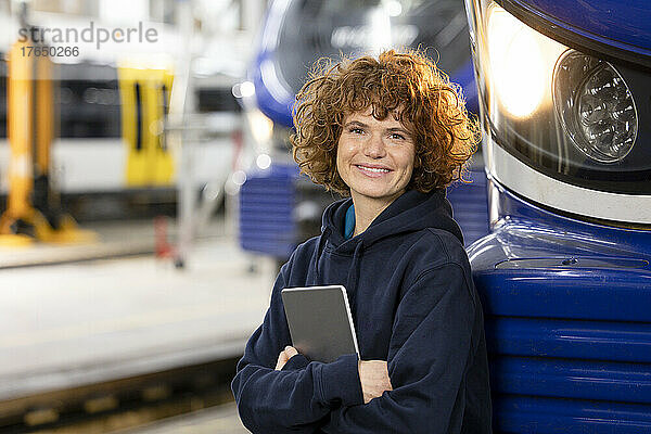 Lächelnder Ingenieur hält Tablet-PC in der Hand und stützt sich auf die Einschienenbahn in der Fabrik