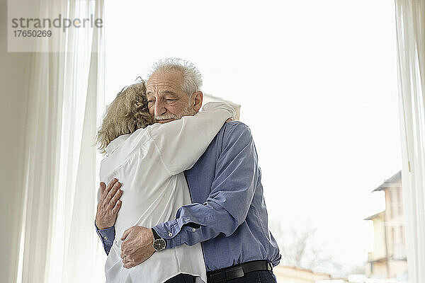 Älteres Paar umarmt sich zu Hause am Fenster