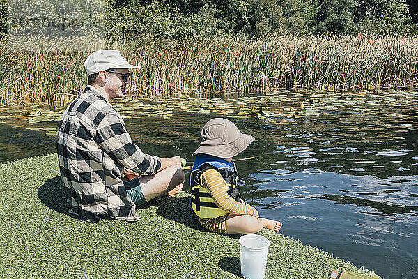 Vater und kleiner Sohn angeln an einem sonnigen Tag im Fluss