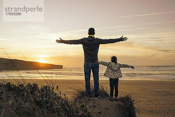 Sorgloser Vater und Tochter stehen mit ausgestreckten Armen auf einer Sanddüne am Strand