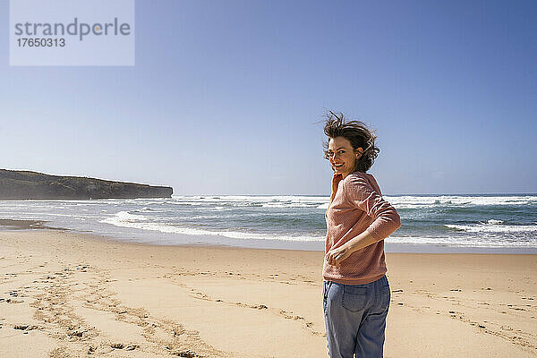 Glückliche Frau  die an einem sonnigen Tag am Strand in Richtung Meer rennt