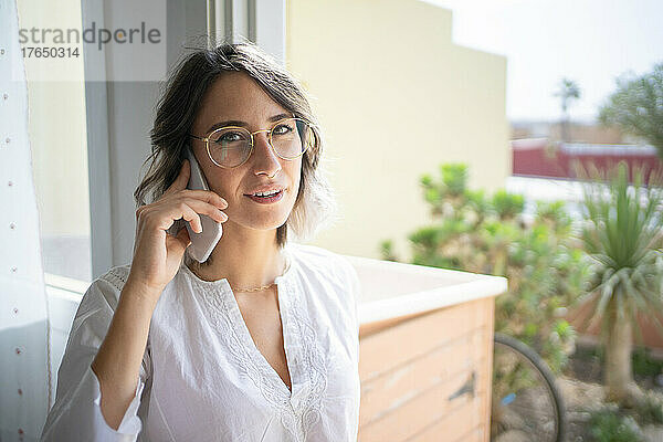 Junge Frau mit Brille telefoniert zu Hause