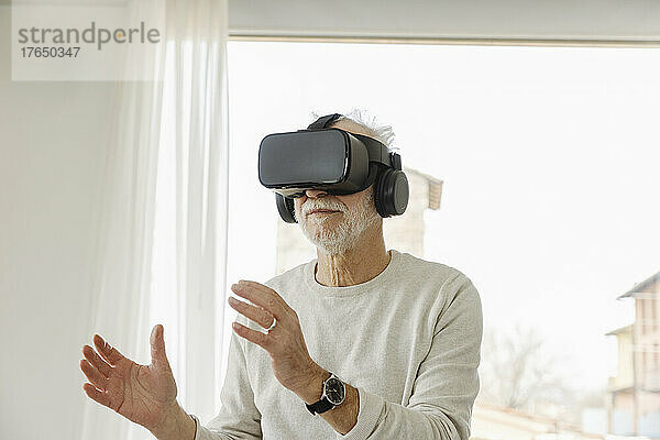 Älterer Mann mit Virtual-Reality-Simulator gestikuliert vor dem Fenster