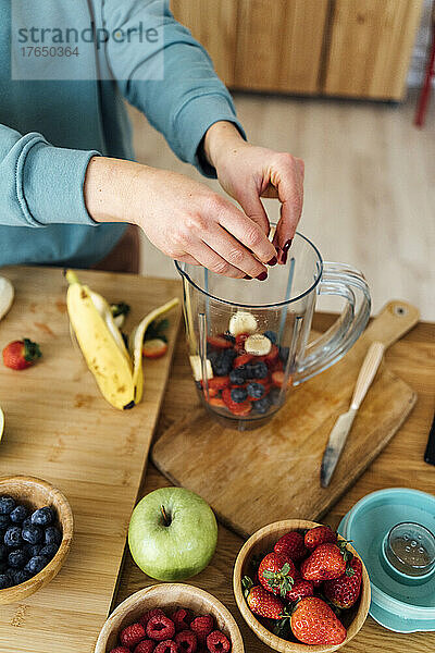 Frau legt frisch gehackte Früchte in den Mixer am Tisch in der Küche