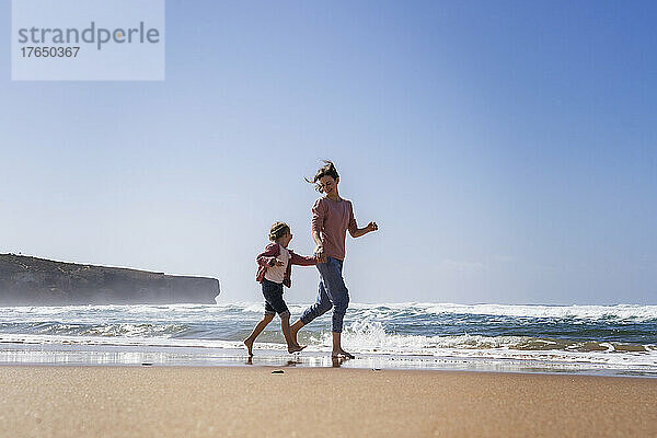 Glückliche Mutter und Tochter laufen an einem sonnigen Tag am Strand