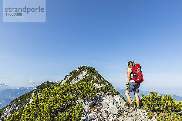 Frau mit Rucksack blickt an sonnigem Tag auf den Berg