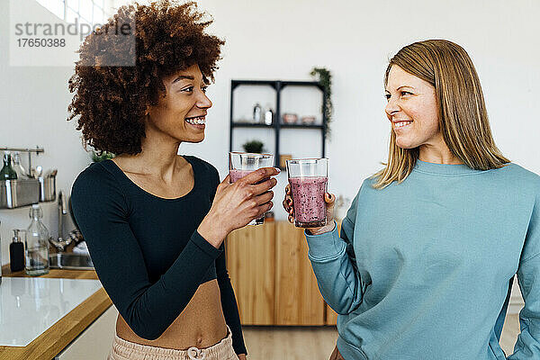 Glückliche Frau toastet in der heimischen Küche ein Glas Smoothie